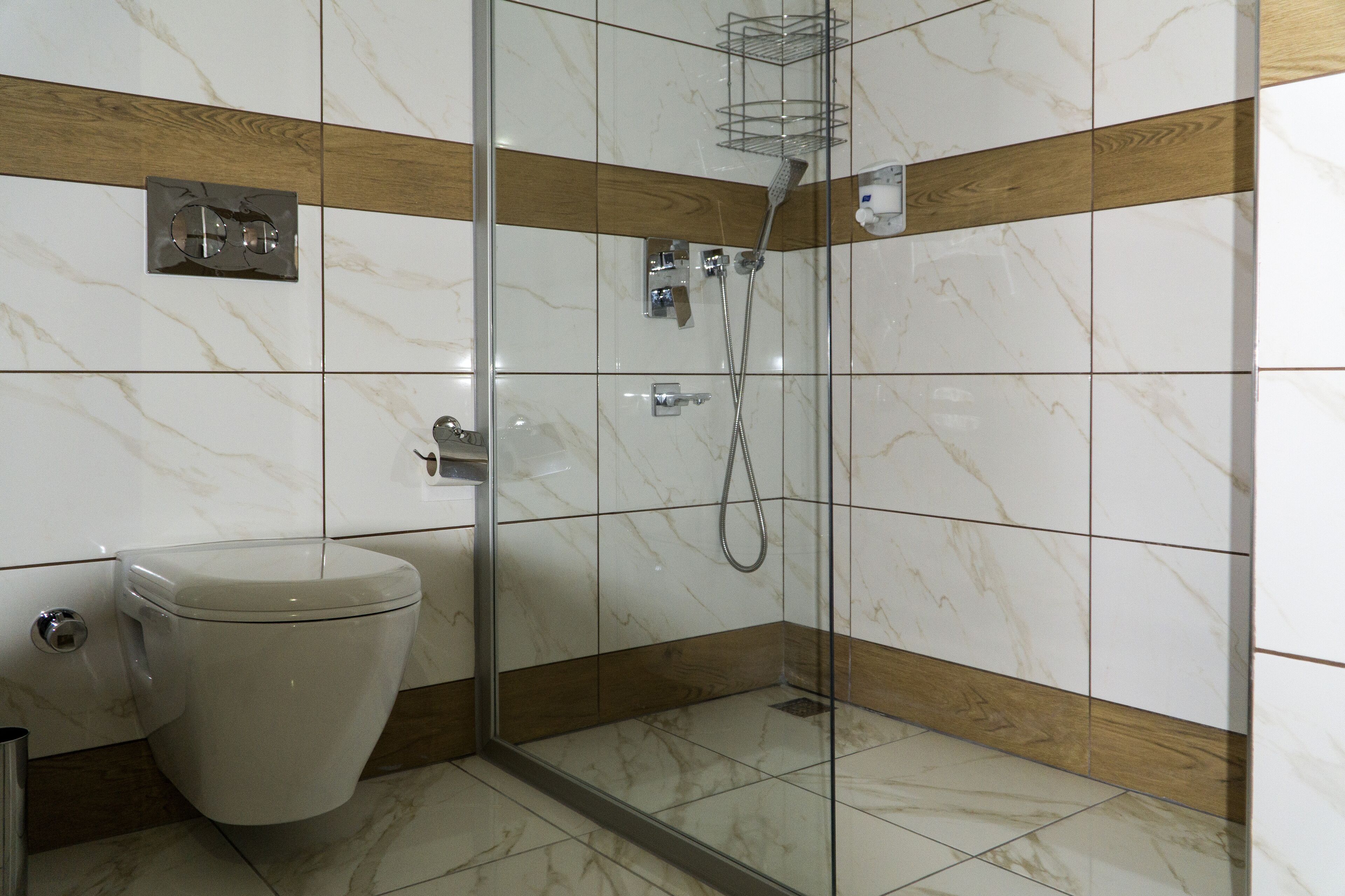 Een moderne badkamer met een douche met glazen wand, een toilet en marmeren tegels.