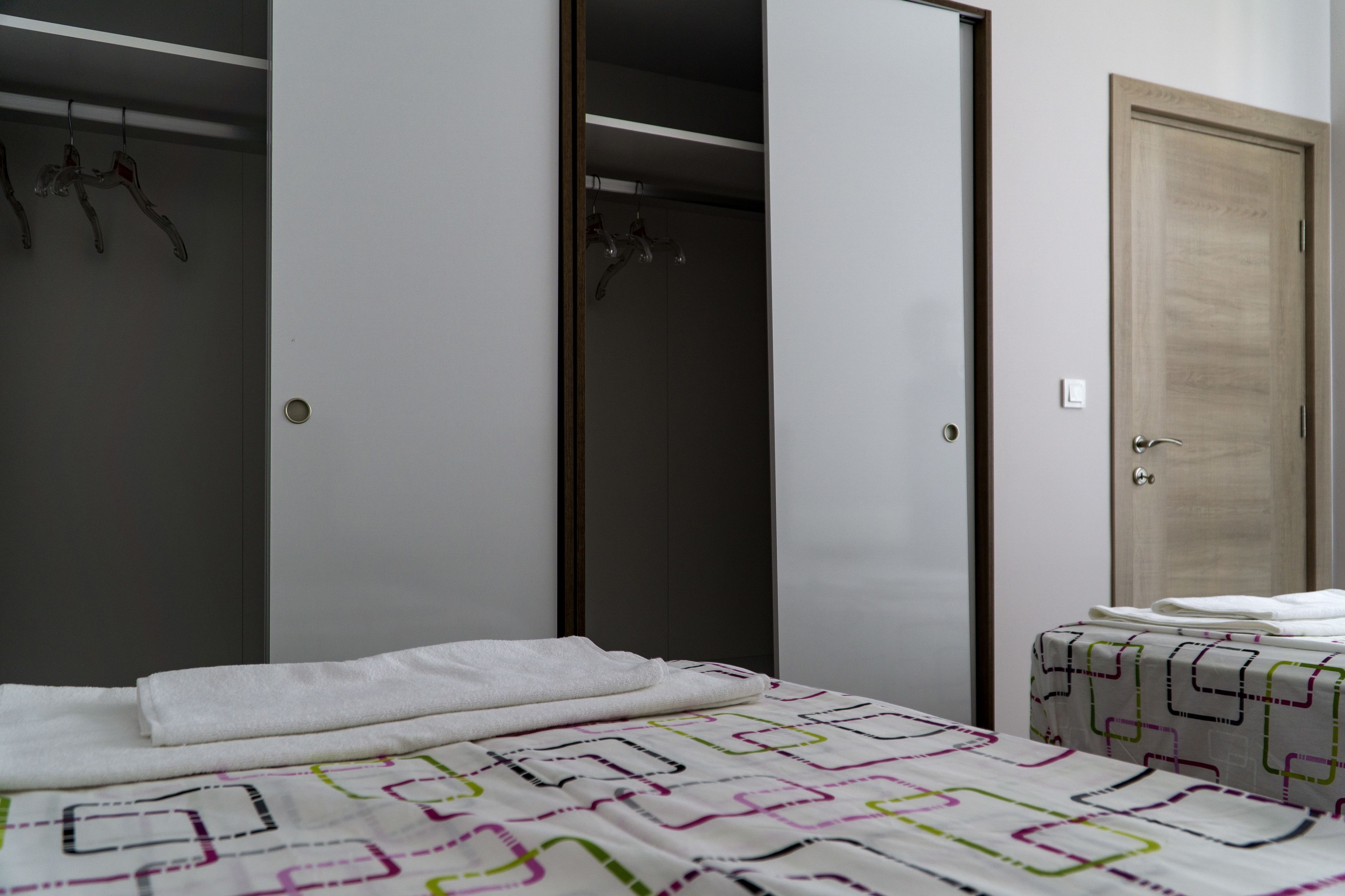 A bedroom with a bed, a closet with hanging clothes, and a door.
