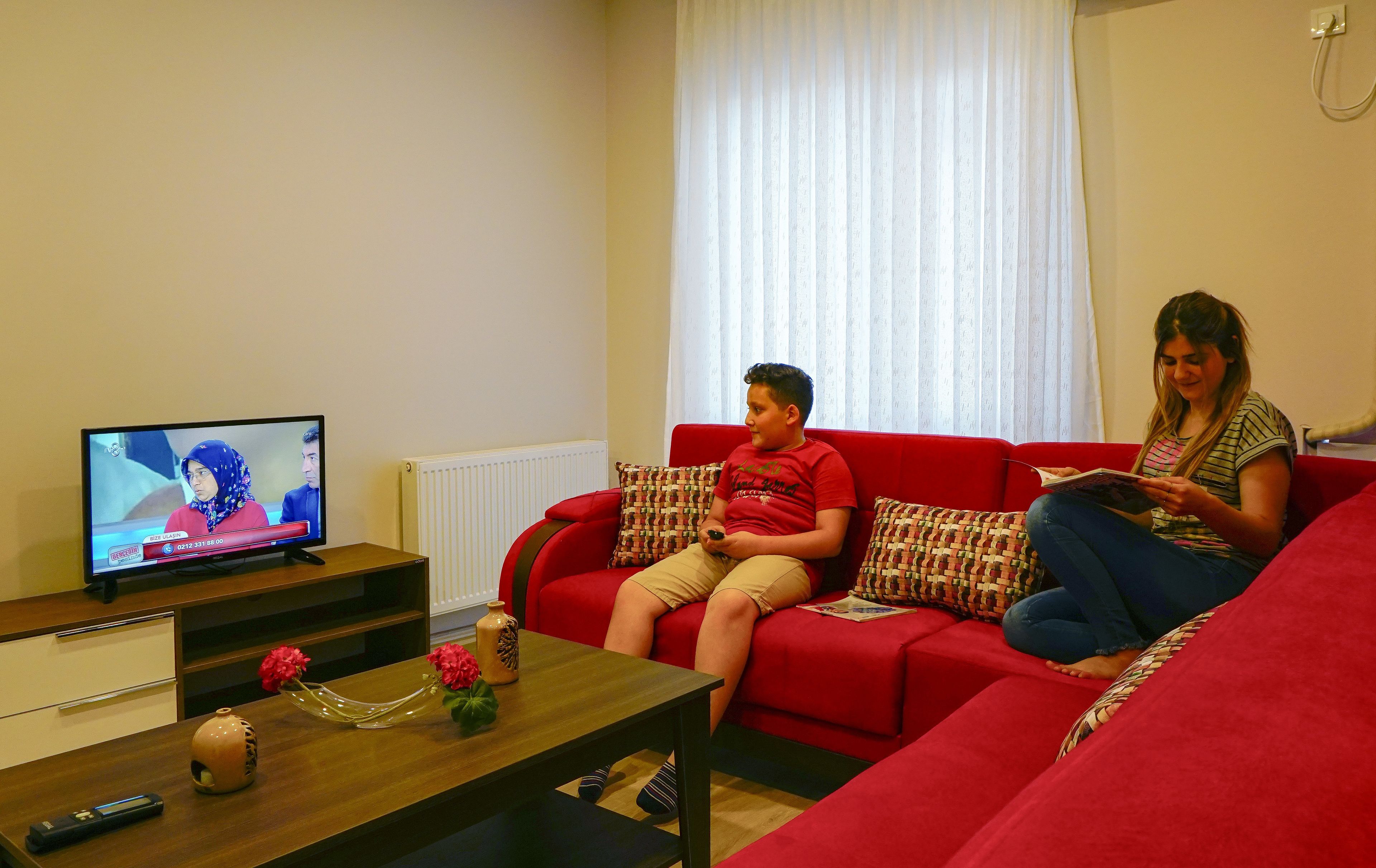 A living room with a red sofa, a wooden coffee table, and a television displaying a news program.