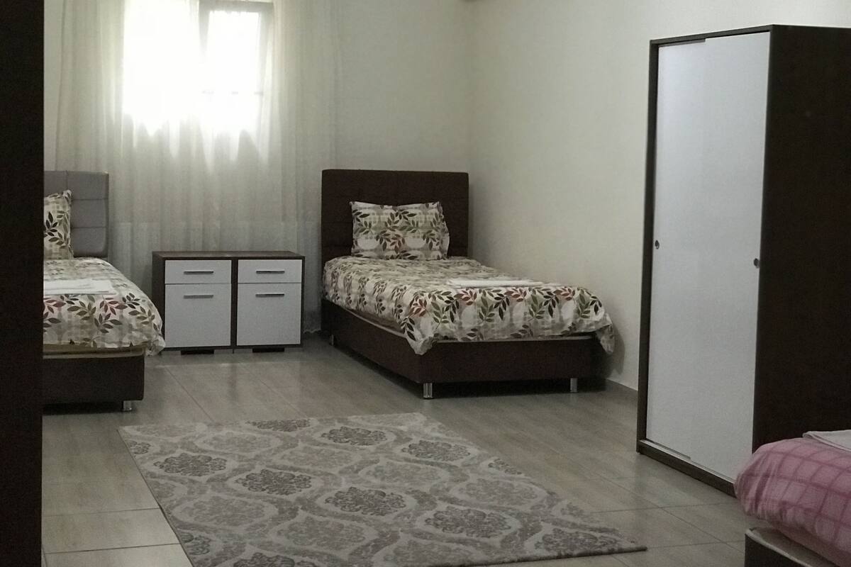 A bedroom with two beds, a wardrobe, a desk, and a window with curtains.