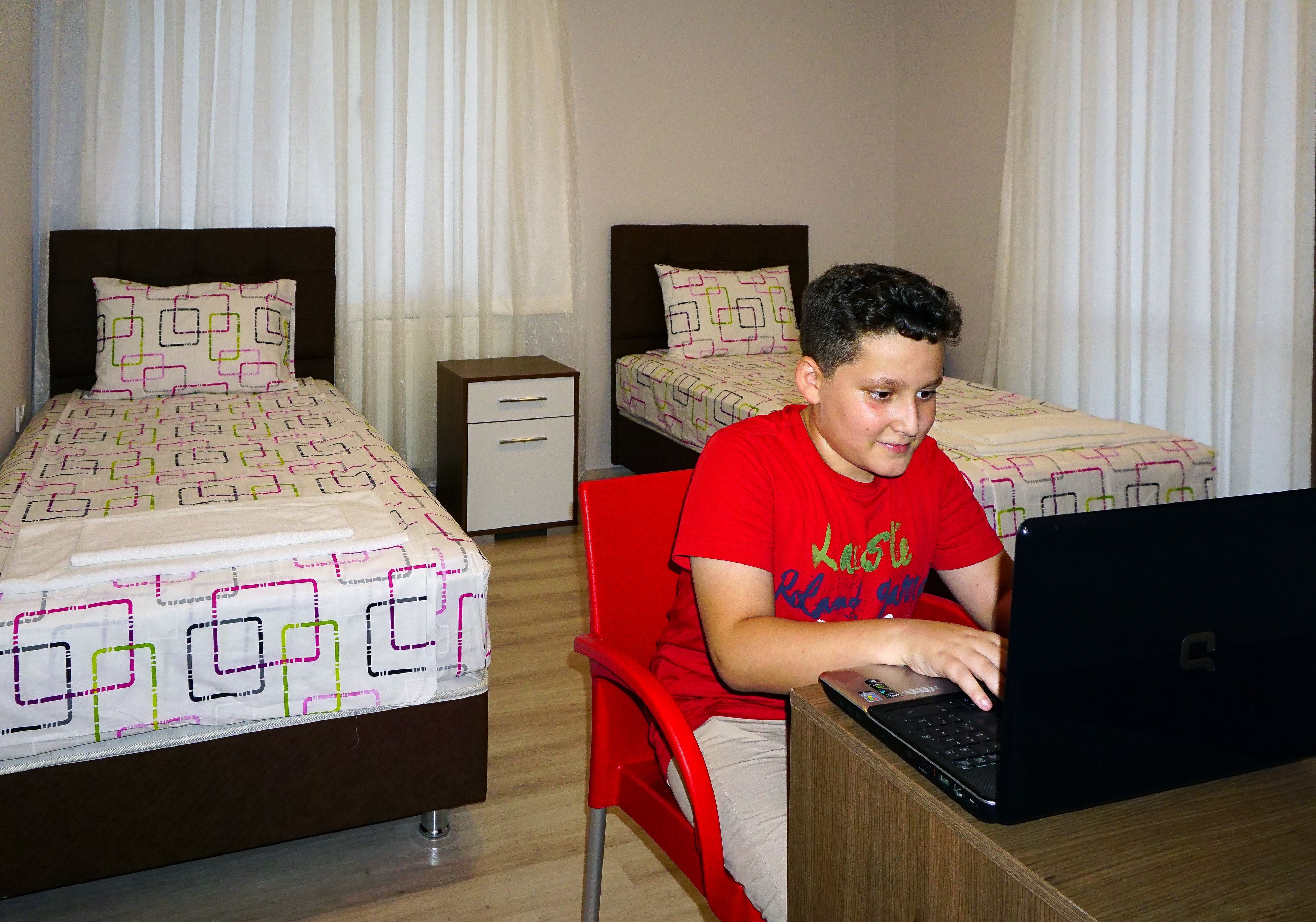 A hotel room with two beds, a desk with a laptop, and a chair.