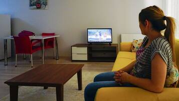 A living room with a sofa, a coffee table, a TV, and a dining area with chairs and a table.