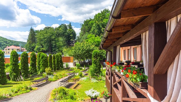A balcony with a wooden railing, a garden with various plants and flowers, and a view of a residential area with houses and trees. - Fantasia Hotel (Poliana)