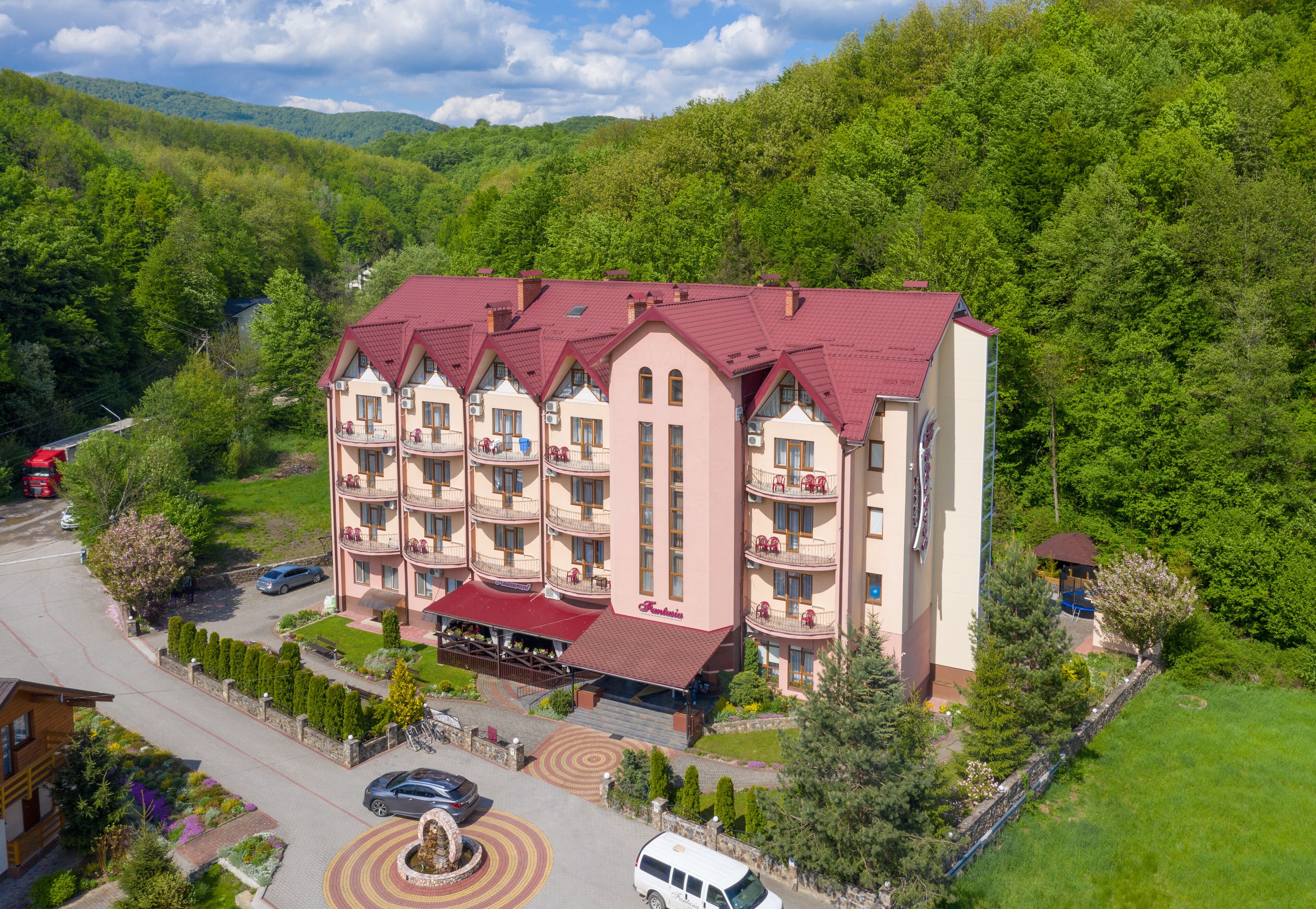 A multi-story hotel with a red roof, surrounded by lush greenery and hills.
