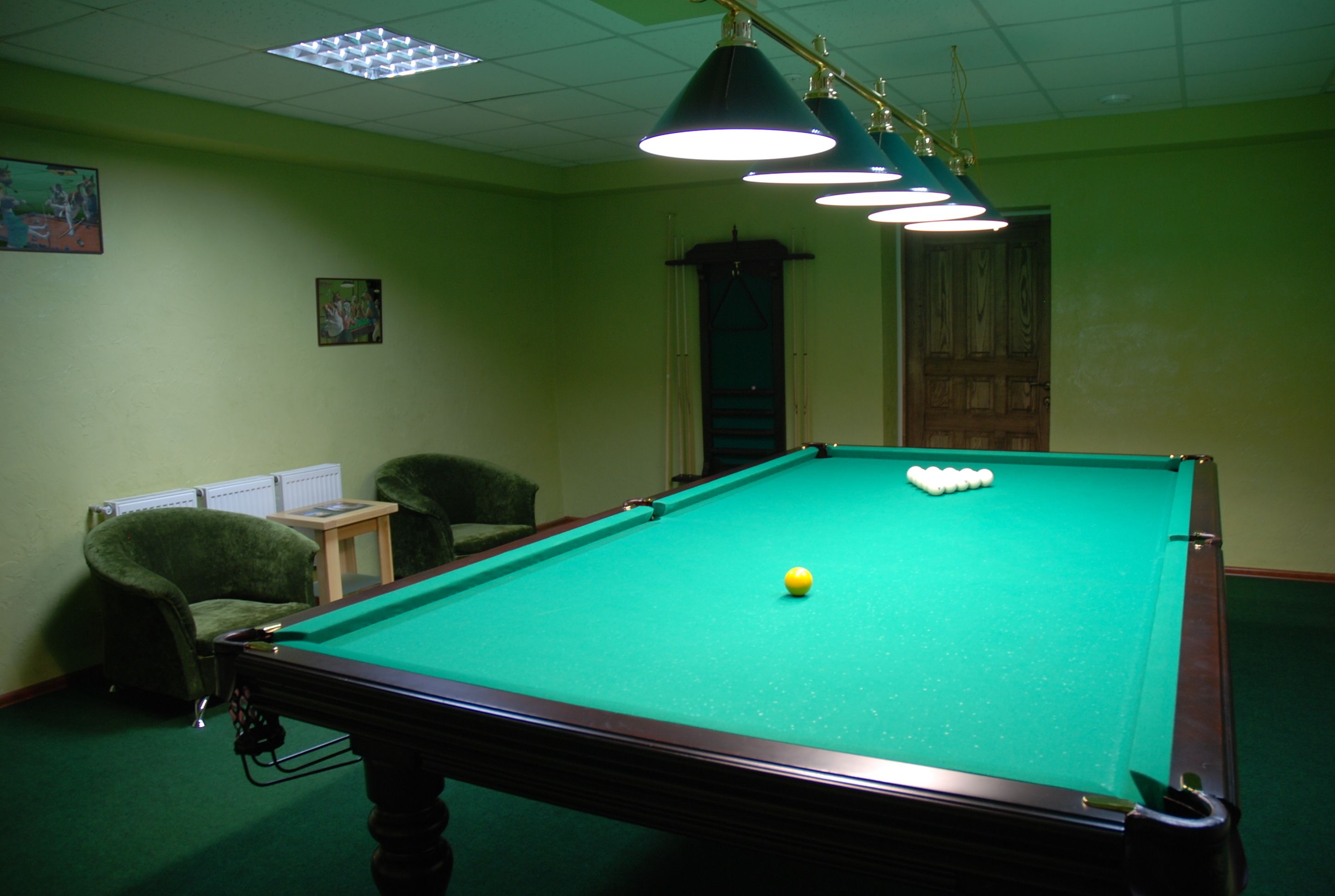 Une table de billard avec des billes, une chaise et un éclairage au plafond, dans une pièce aux murs verts.