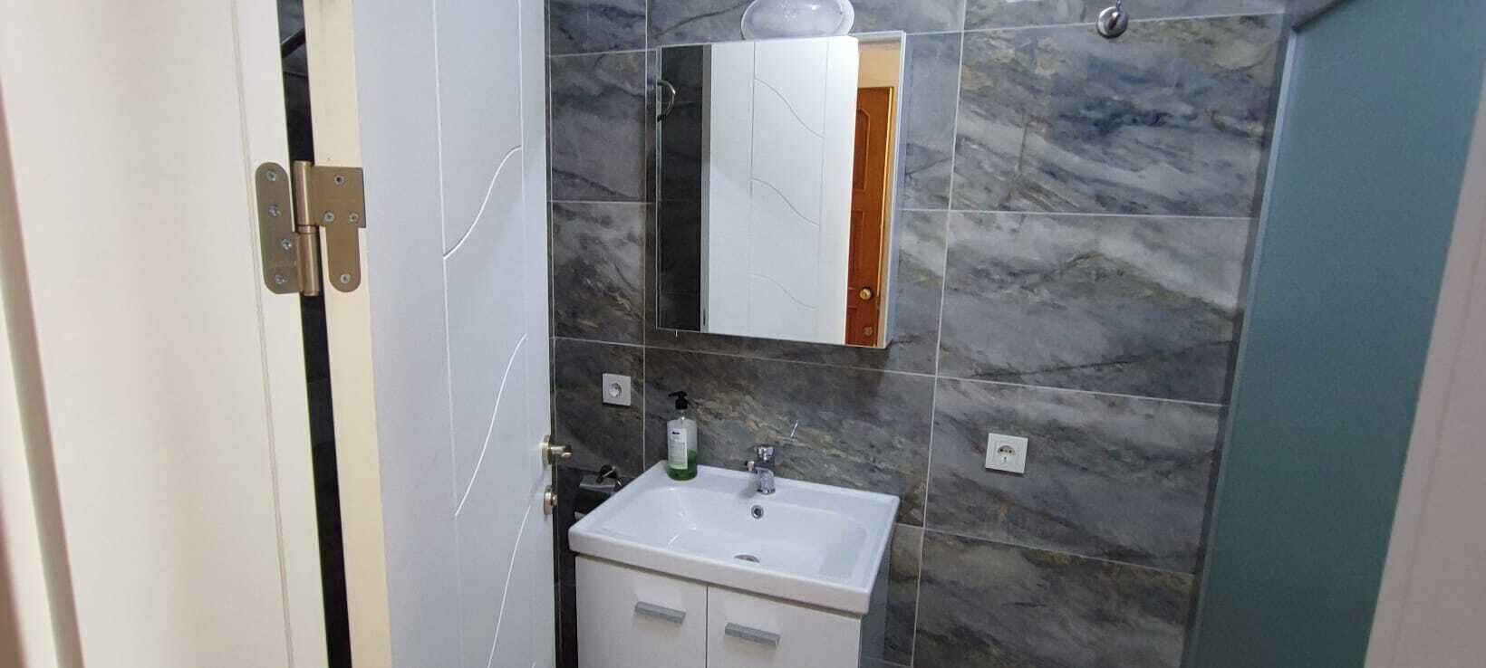 A bathroom with a white sink, a mirror, and marble tiles.