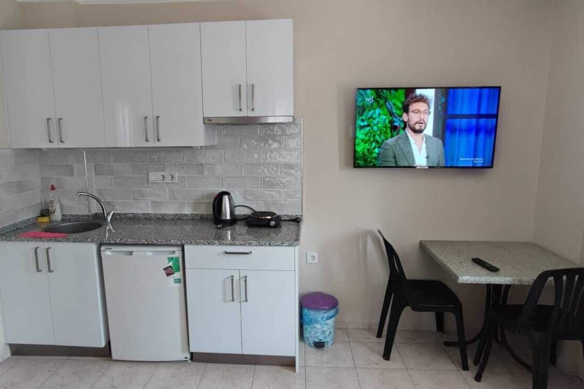 A compact kitchen with white cabinets, a small refrigerator, a coffee maker, and a TV on the wall.