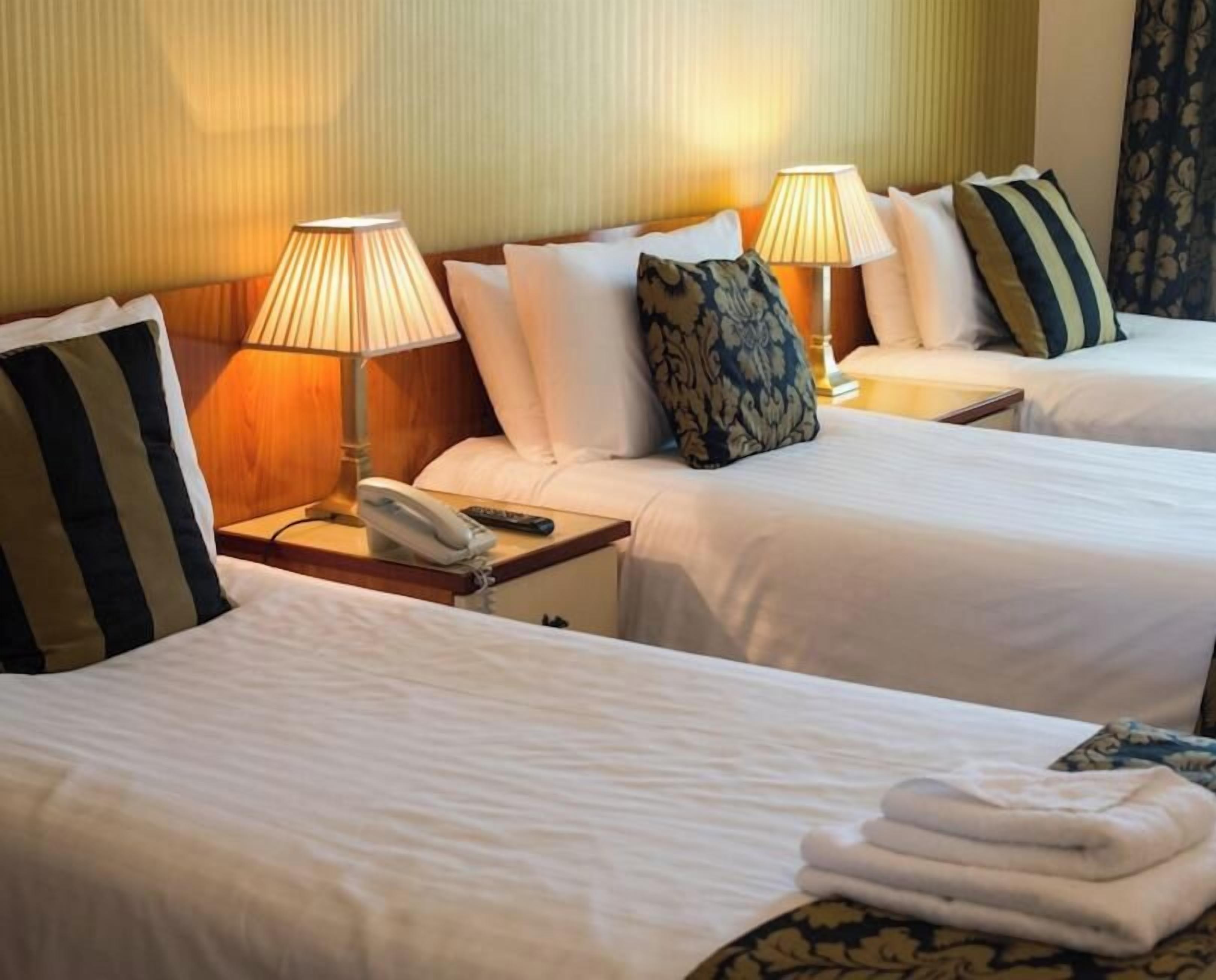 A hotel room with two beds, bedside lamps, a telephone, and a folded towel on the bed.