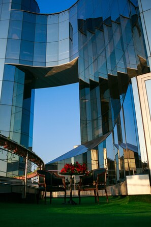 Een modern gebouw met glazen spiegelramen en een gazon met terrasplekken.