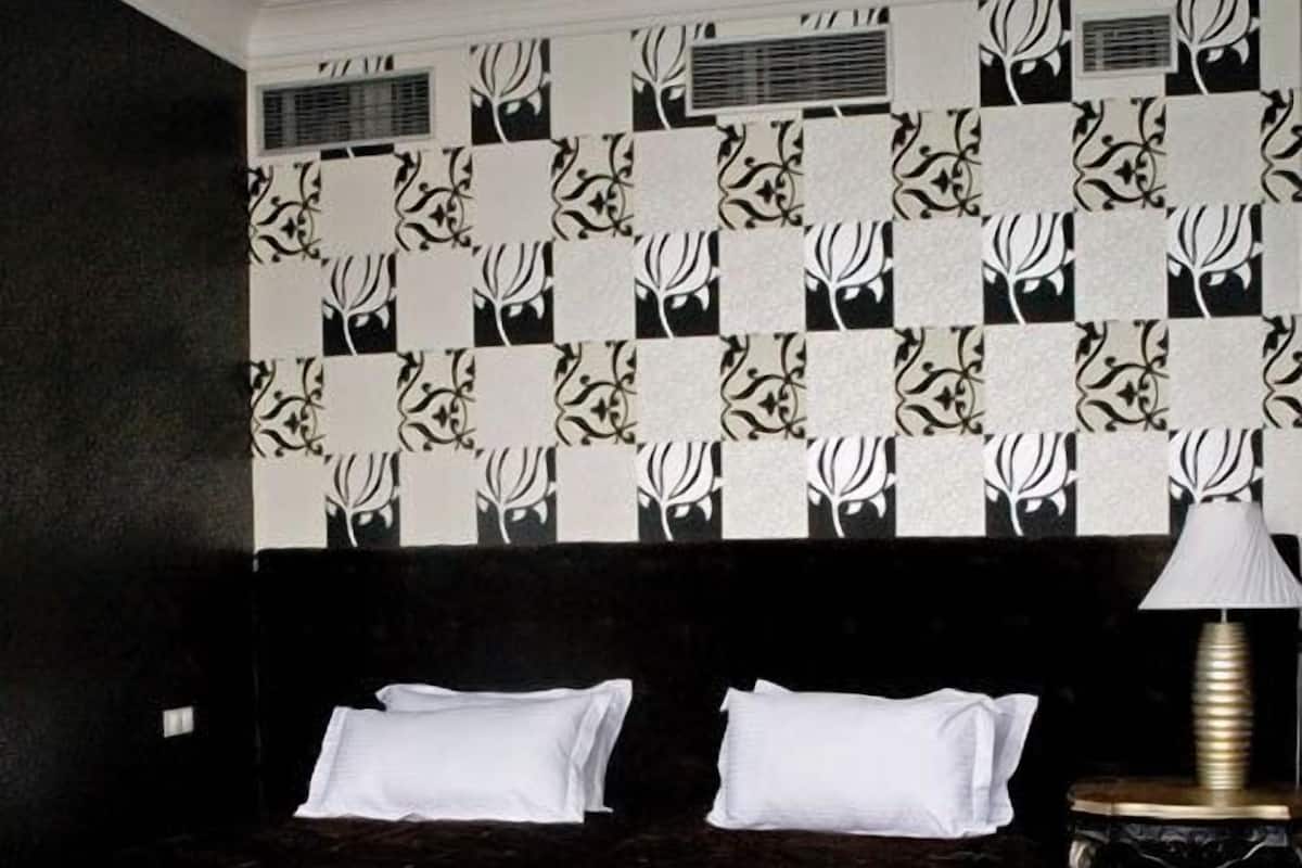 A bedroom with a patterned wallpaper, a dark headboard, white pillows, and a bedside lamp.