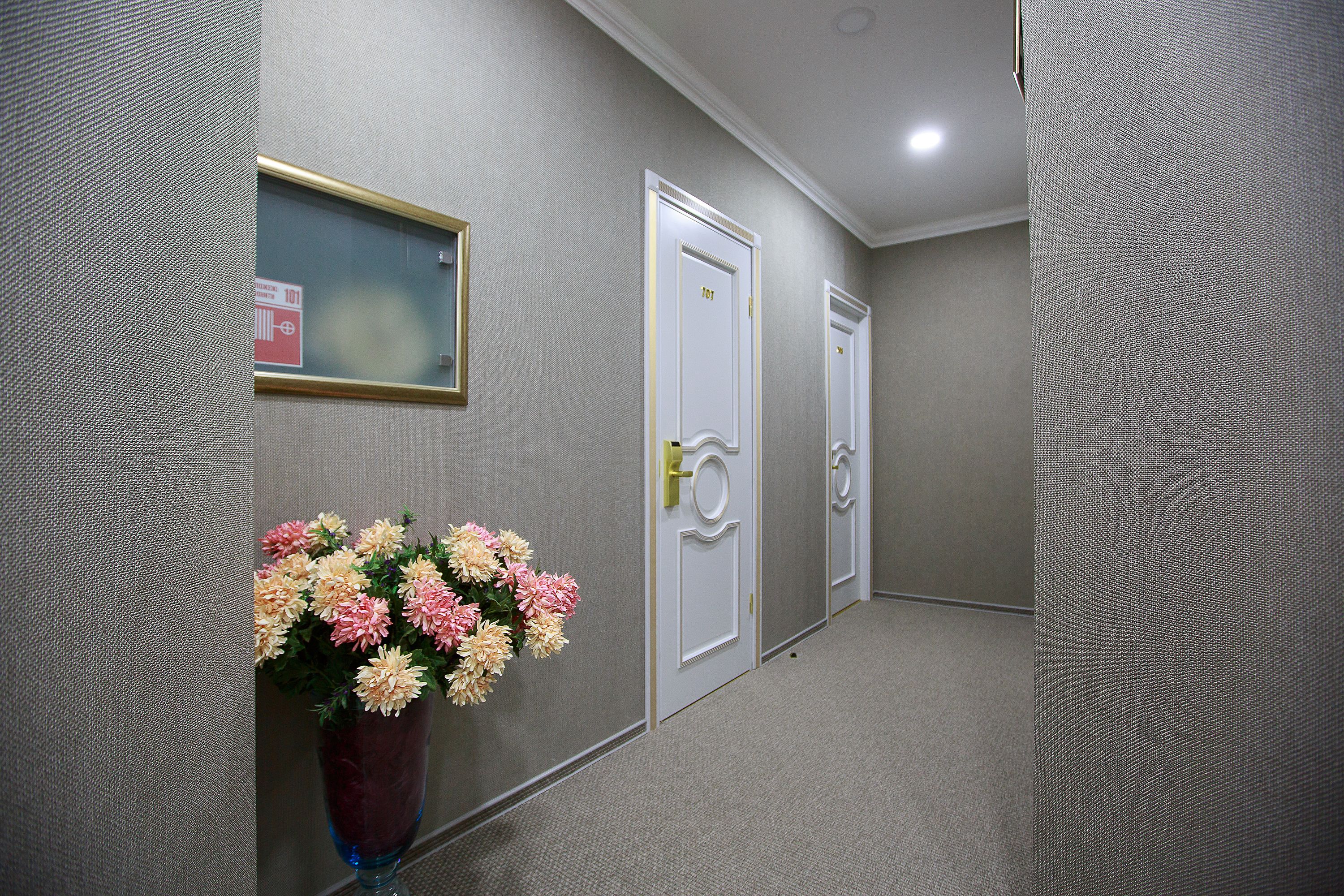 Un pasillo con dos puertas blancas, un cartel en la pared y un jarrón de flores.