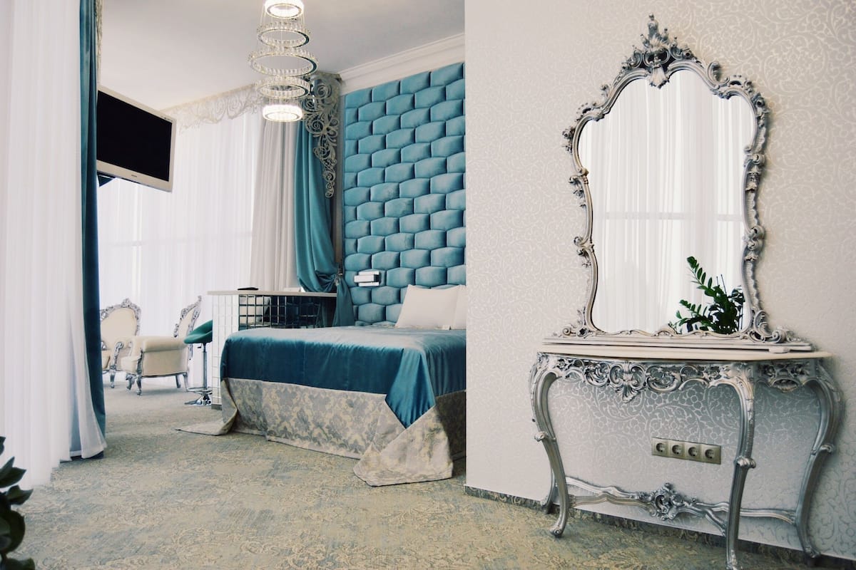 A bedroom with a large bed, a vanity with a mirror, and a television on the wall.