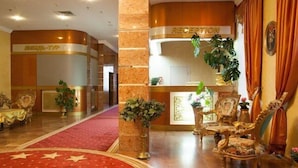 Un área de recepción con alfombra roja, sillones ornamentados y un mostrador de recepción.