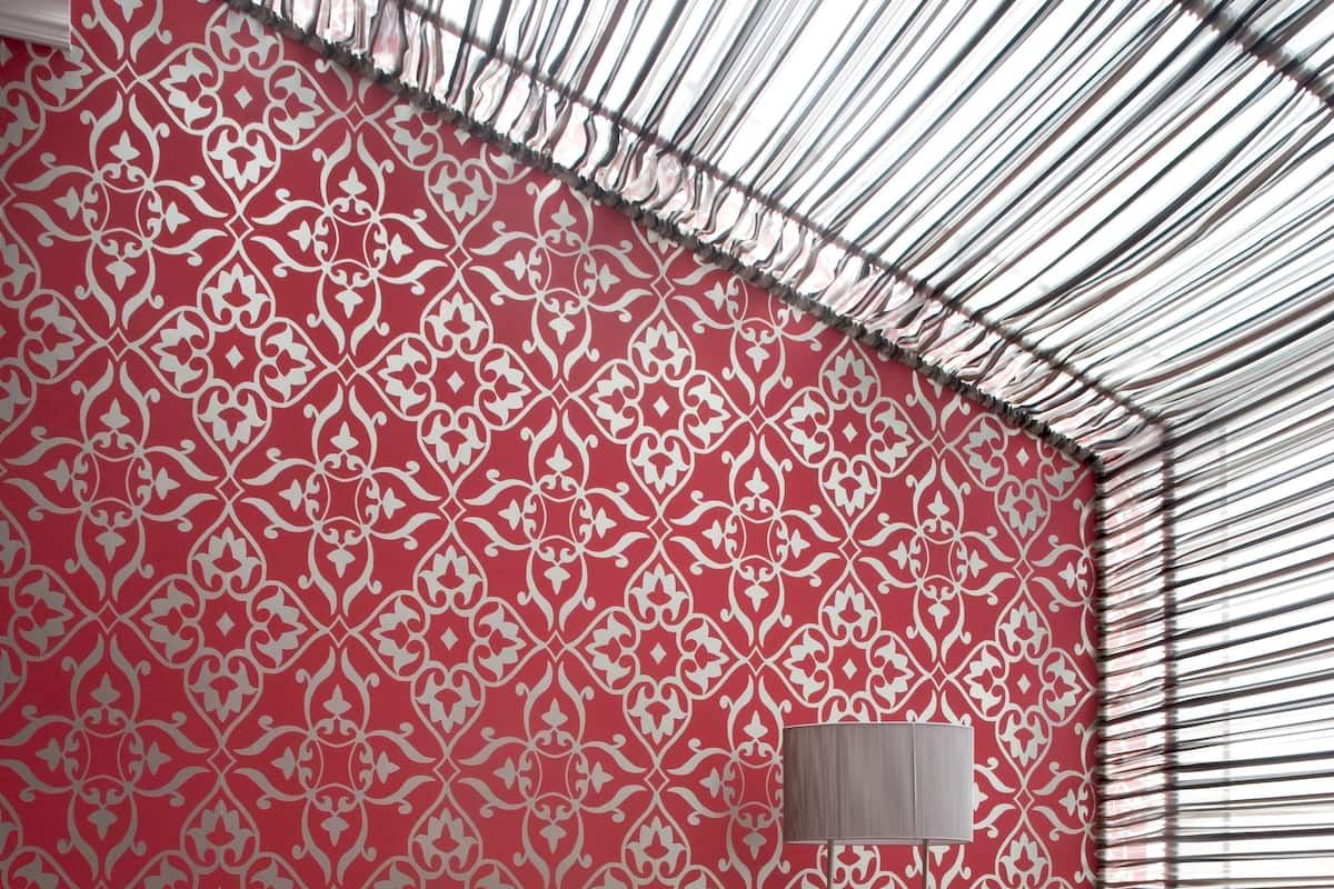 A room with a red sofa, grey cushions, a silver coffee table, and a patterned red and white wallpaper.