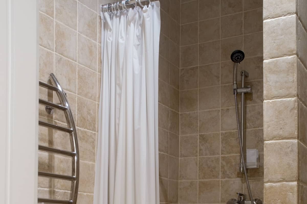 A shower area with beige tiles, a white shower curtain, and a handheld showerhead.