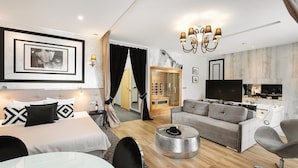 A modern hotel room with a bed, a sofa, a dining table, and a kitchen area.