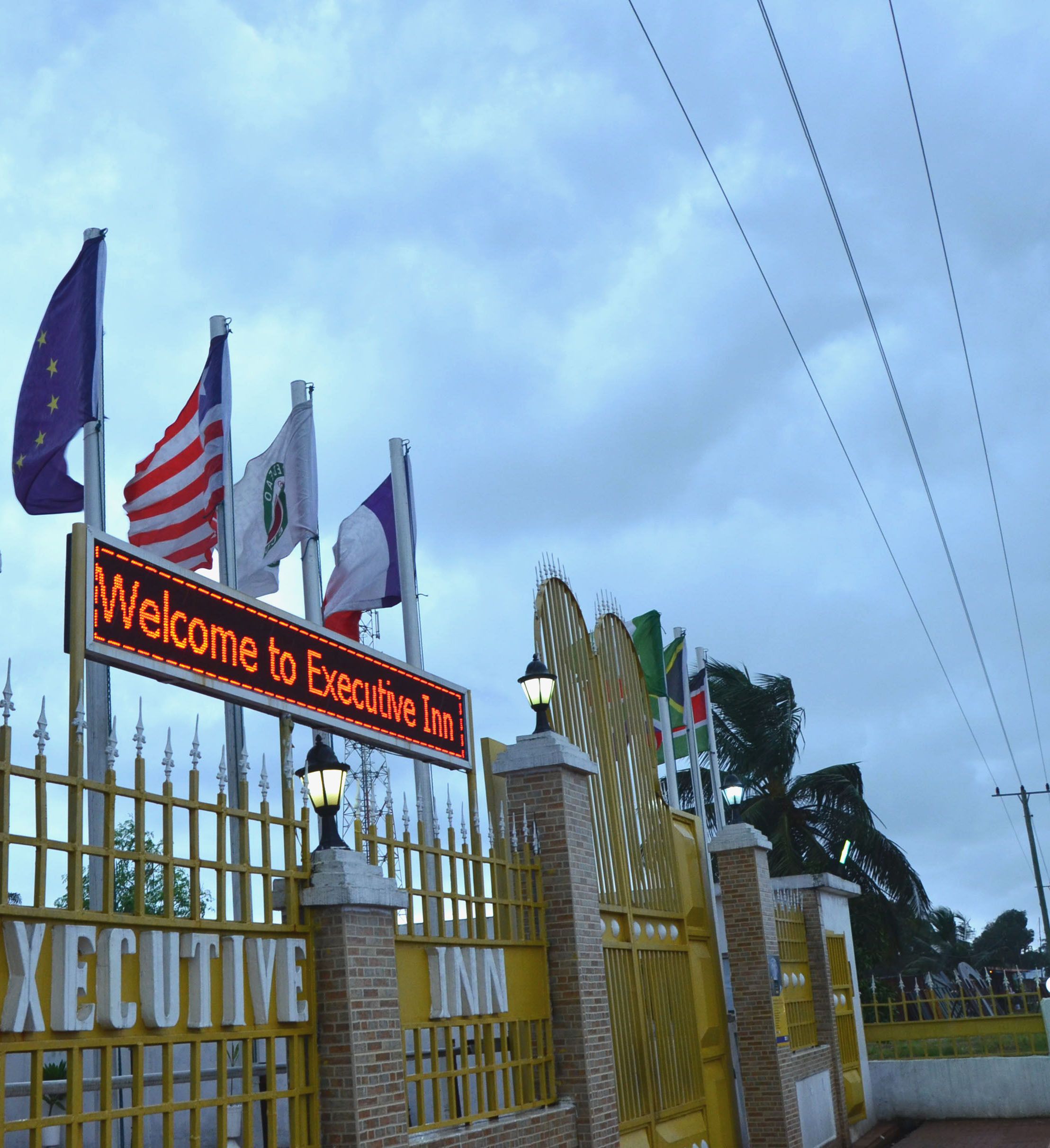 A sign welcoming visitors to the Executive Inn, featuring multiple national flags and a gated entrance.