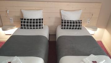 Duas camas de solteiro com roupa de cama branca e cinza, almofadas xadrez preto e branco e cabeceira de madeira.