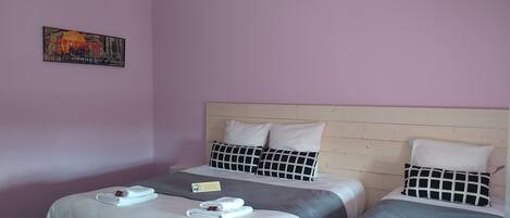 Habitación de hotel con dos camas, cada una con ropa de cama blanca y almohadas a cuadros blanco y negro. Hay una pequeña mesa con un cartel y toallas sobre las camas.