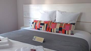 Un lit bien fait, avec des oreillers blancs et colorés, une couverture grise et un petit panneau posé sur le lit.