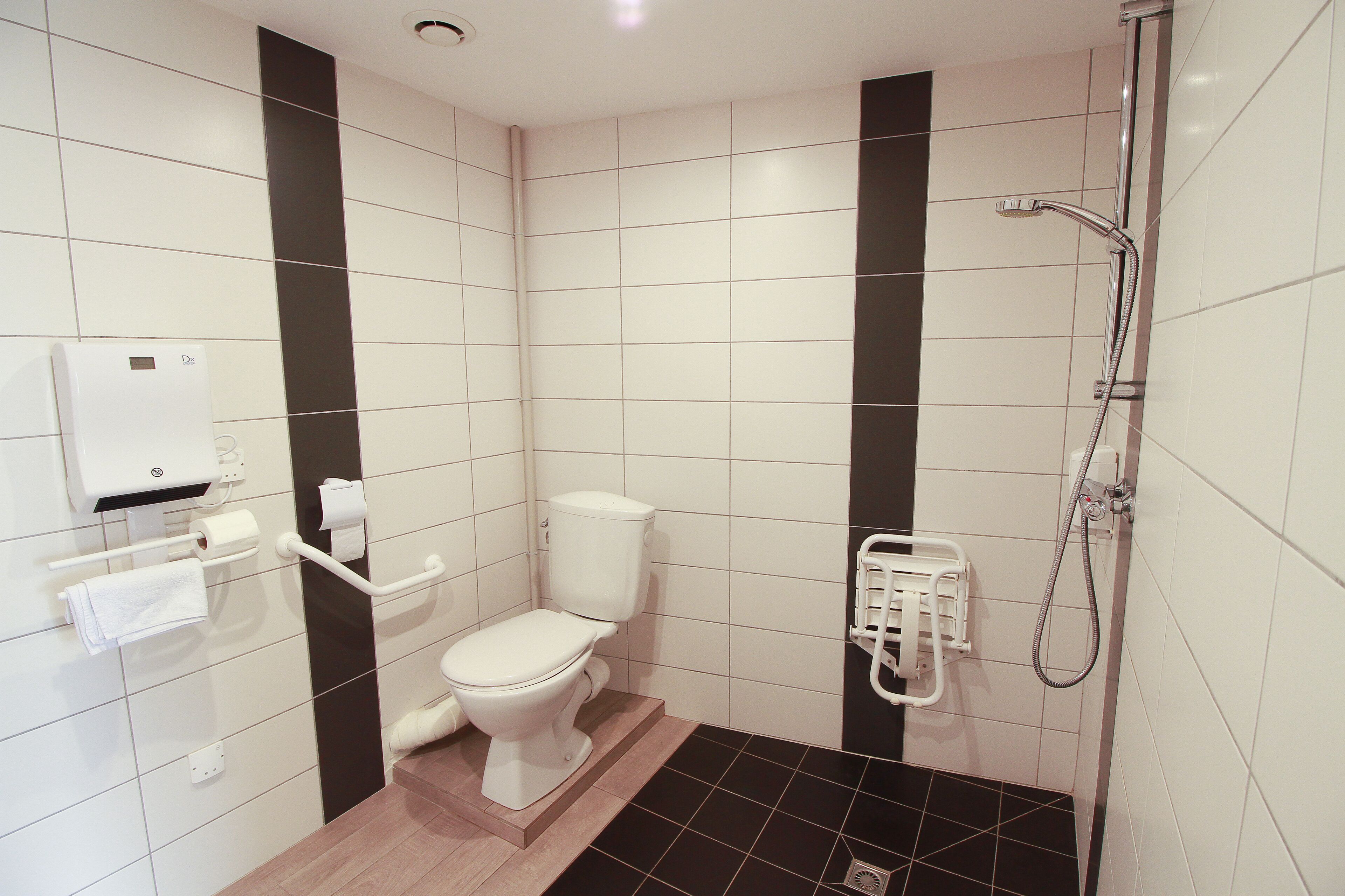 Un baño pequeño y moderno con inodoro, ducha y secador de manos.