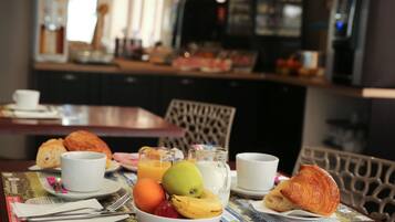 Un desayuno con un bol de fruta, cruasanes y bebidas sobre una mesa.