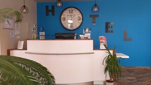 Una reception di un hotel con una grande orologio, una parete blu con la scritta 'HOTEL' e una pianta.