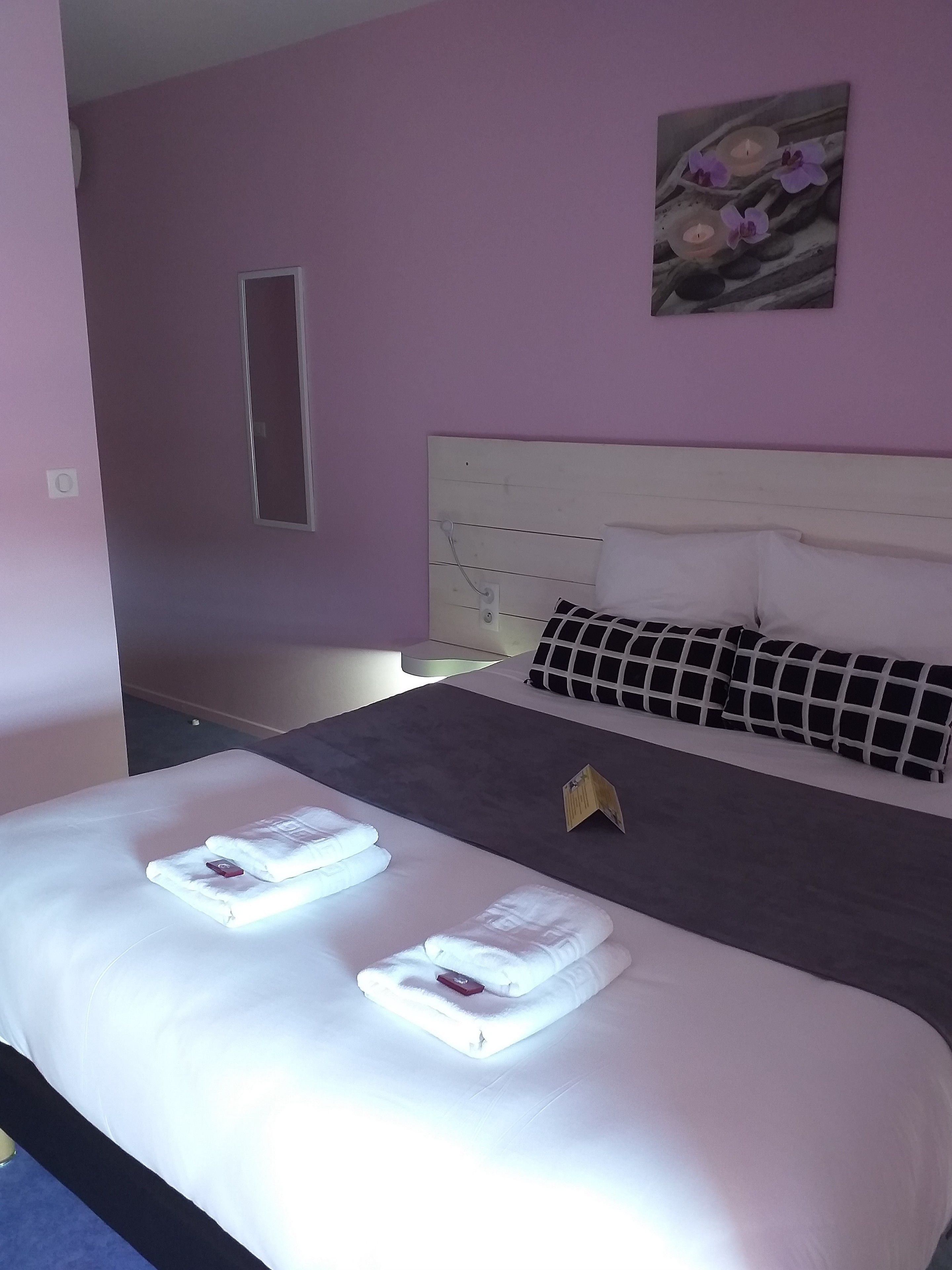 A neatly made bed with white linens and two towels folded on it.
