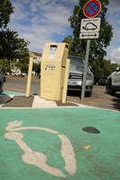Un área de estacionamiento con una estación de carga, un letrero de no estacionar y un carril bici verde.