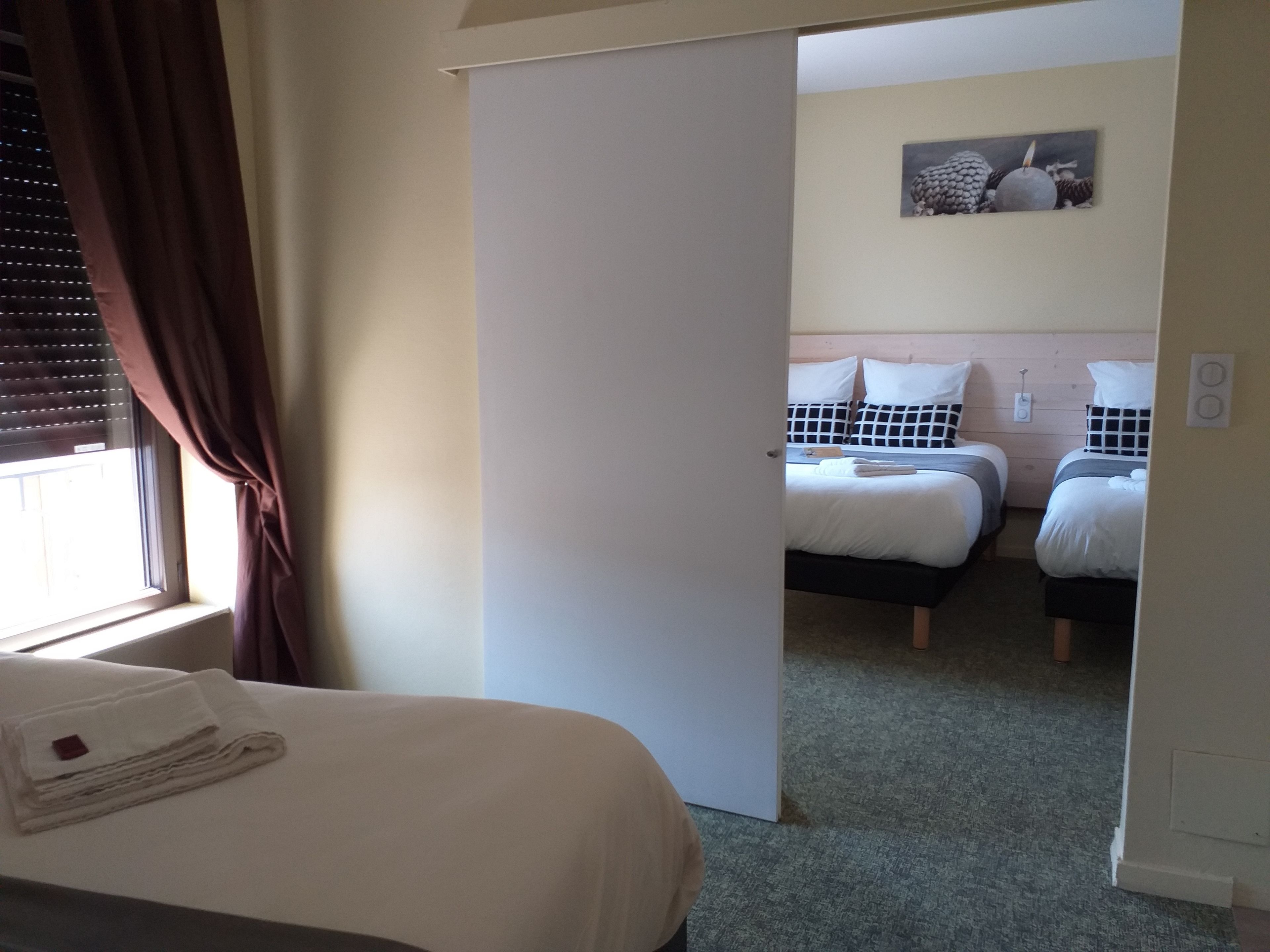 A hotel room with a large bed, two smaller beds, a painting on the wall, and a window with curtains.
