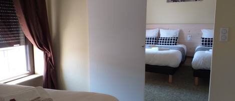 A hotel room with a large bed, two smaller beds, a painting on the wall, and a window with curtains.