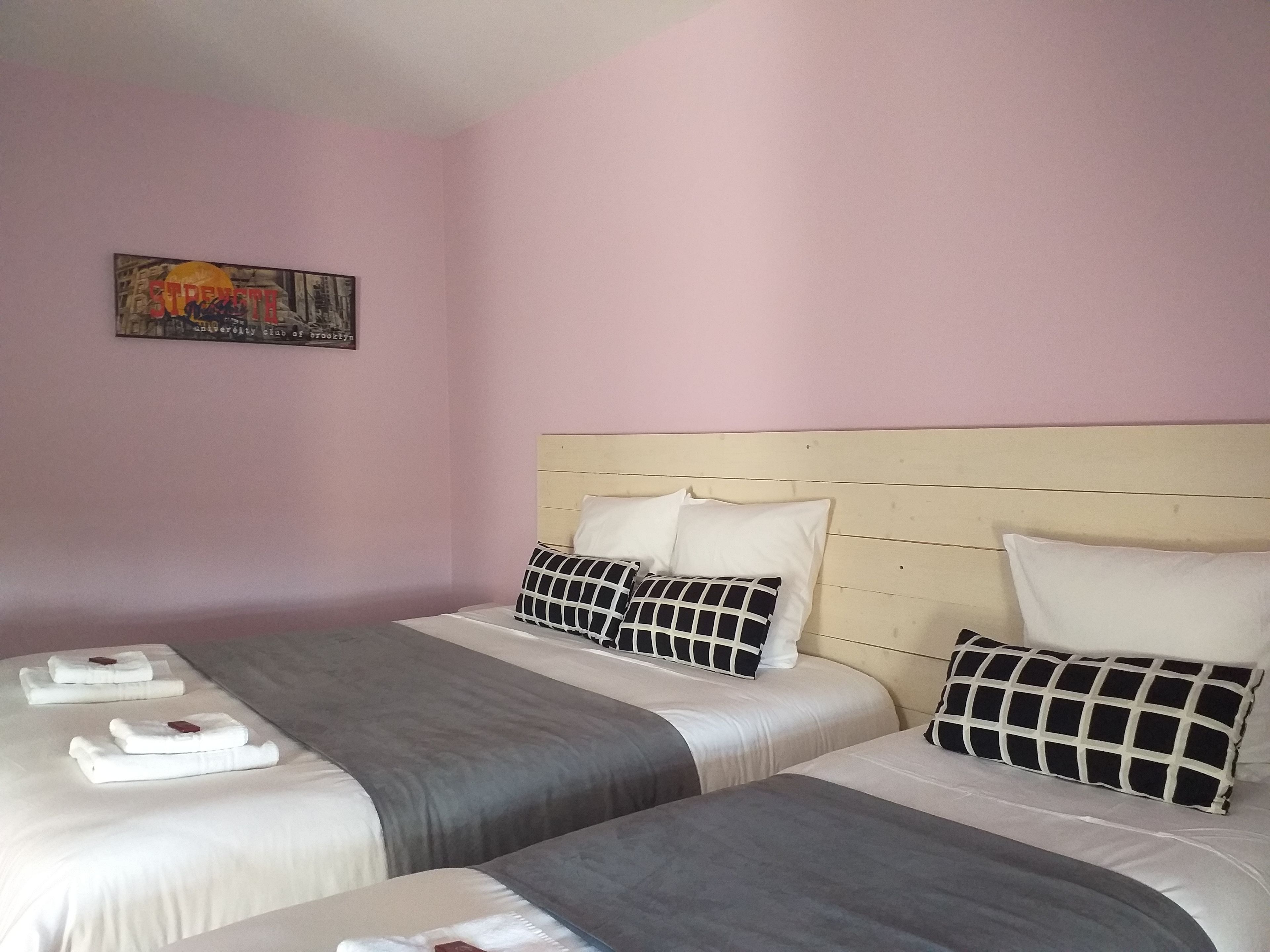 A hotel room with two beds, each with white linens and a grey blanket. There is a painting on the wall above the beds.