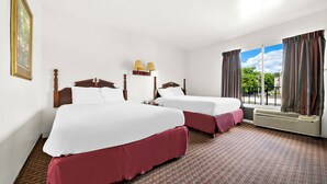 A hotel room with two beds, a large window with curtains, a patterned carpet, and a framed picture on the wall. - Capitol Inn And Suites (Montgomery)