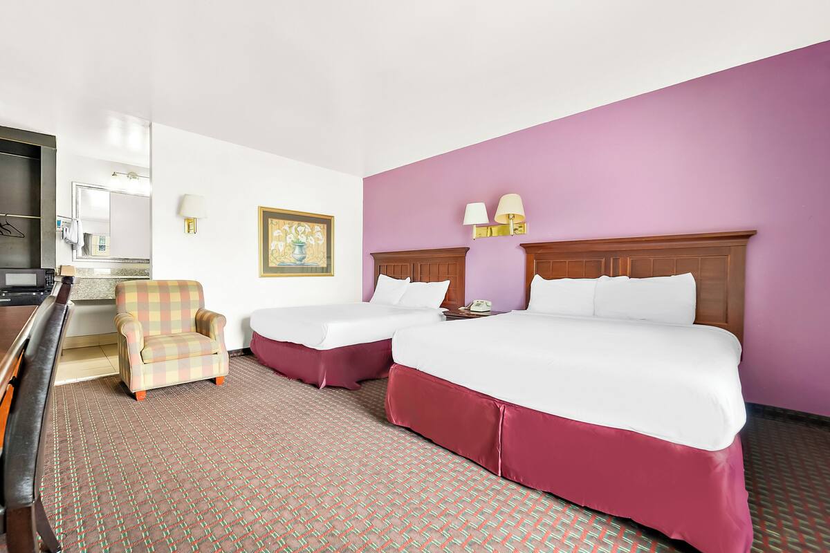 A hotel room with two beds, a chair, a desk, and a television.