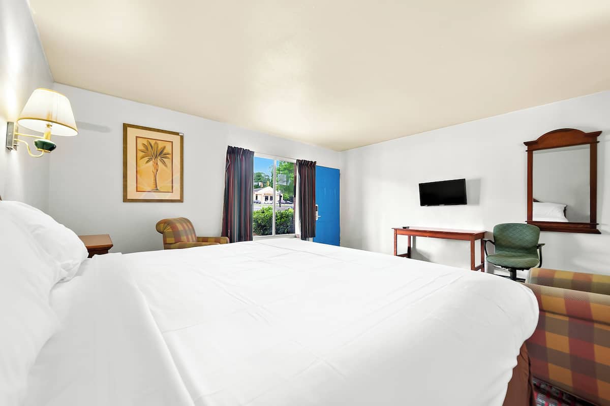 A hotel room with a large bed, a desk, a chair, a television, and a window with curtains.