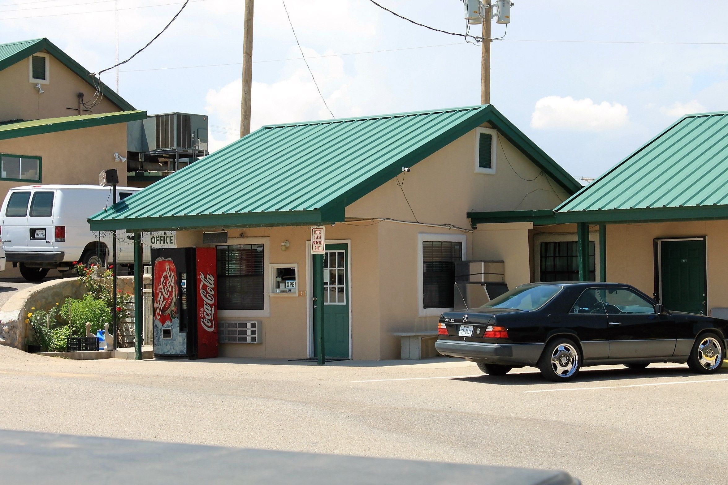 A building with a green roof, a Coca-Cola vending machine, and a sign indicating an office.