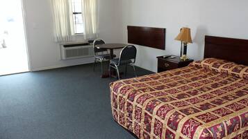 A hotel room with a bed, a desk, a chair, a lamp, and a window with curtains.