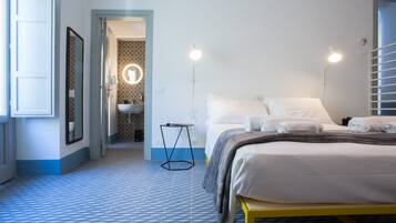 Habitación de hotel con cama, lámparas de noche, una mesita y un baño visible a través de una puerta abierta.