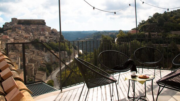 Una terraza con sillas y una mesa, con vistas a un pueblo histórico y una masa de agua.