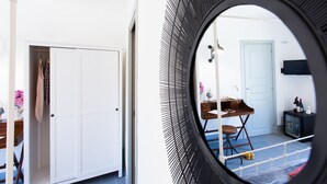 Una habitación con una puerta blanca, un espejo redondo, una mesa de madera, una silla, un mueble pequeño y un televisor.