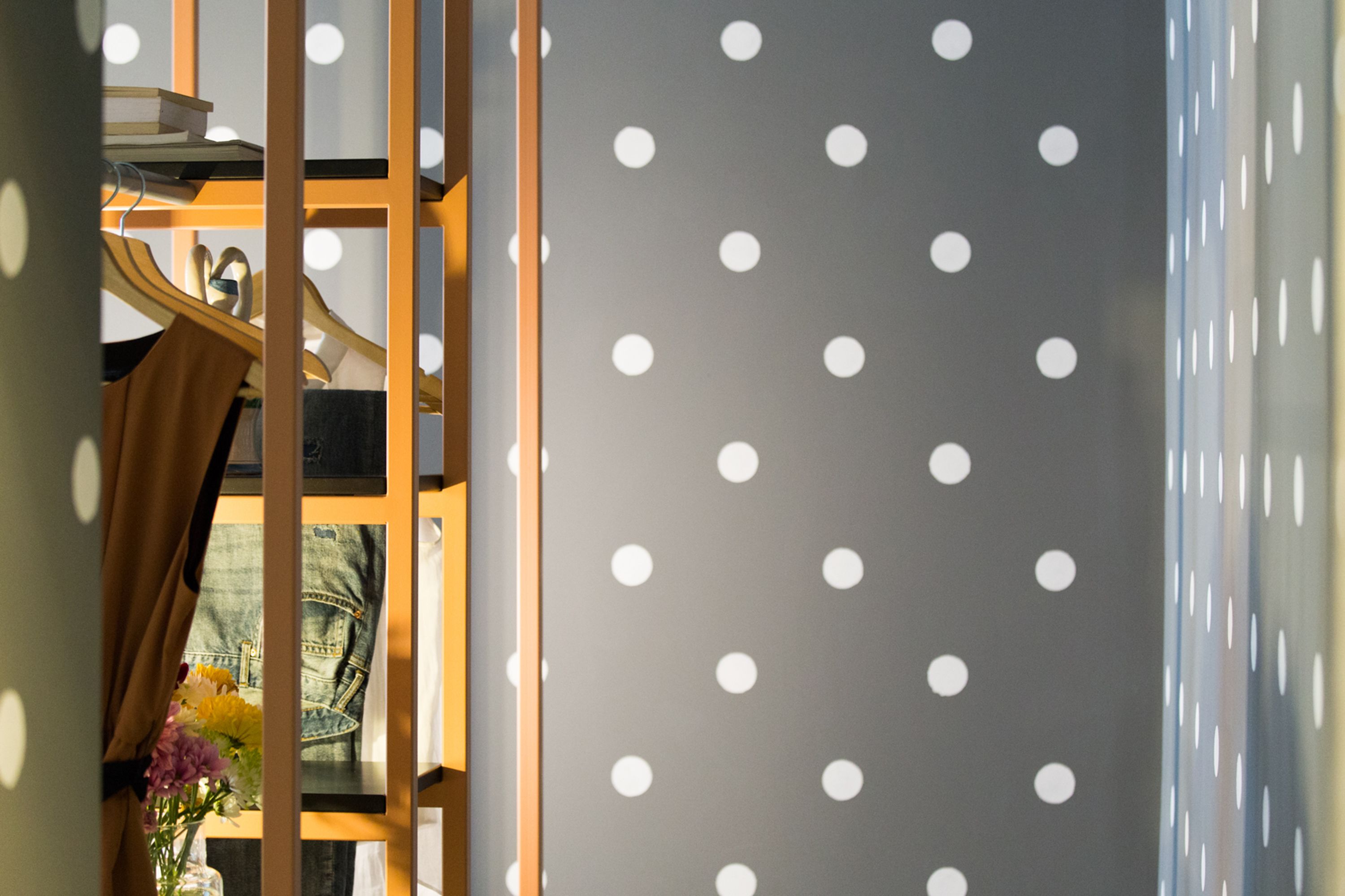 A room with a polka dot wall, a wooden shelf with books and a pair of scissors, and a denim jacket hanging on the wall.