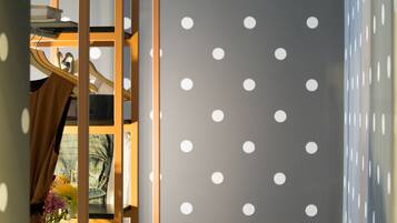 A room with a polka dot wall, a wooden shelf with books and a pair of scissors, and a denim jacket hanging on the wall.