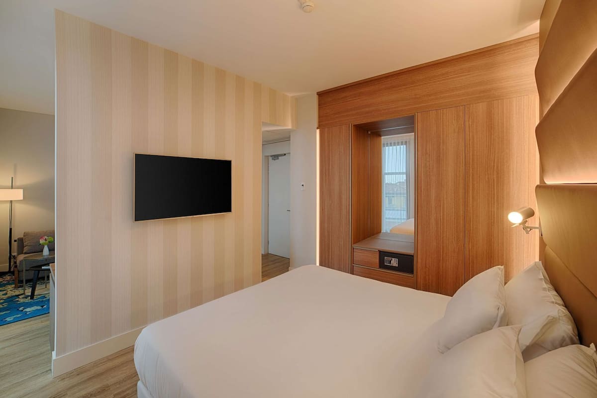 A hotel room with a bed, a TV mounted on the wall, a wooden cabinet, and a mirror.