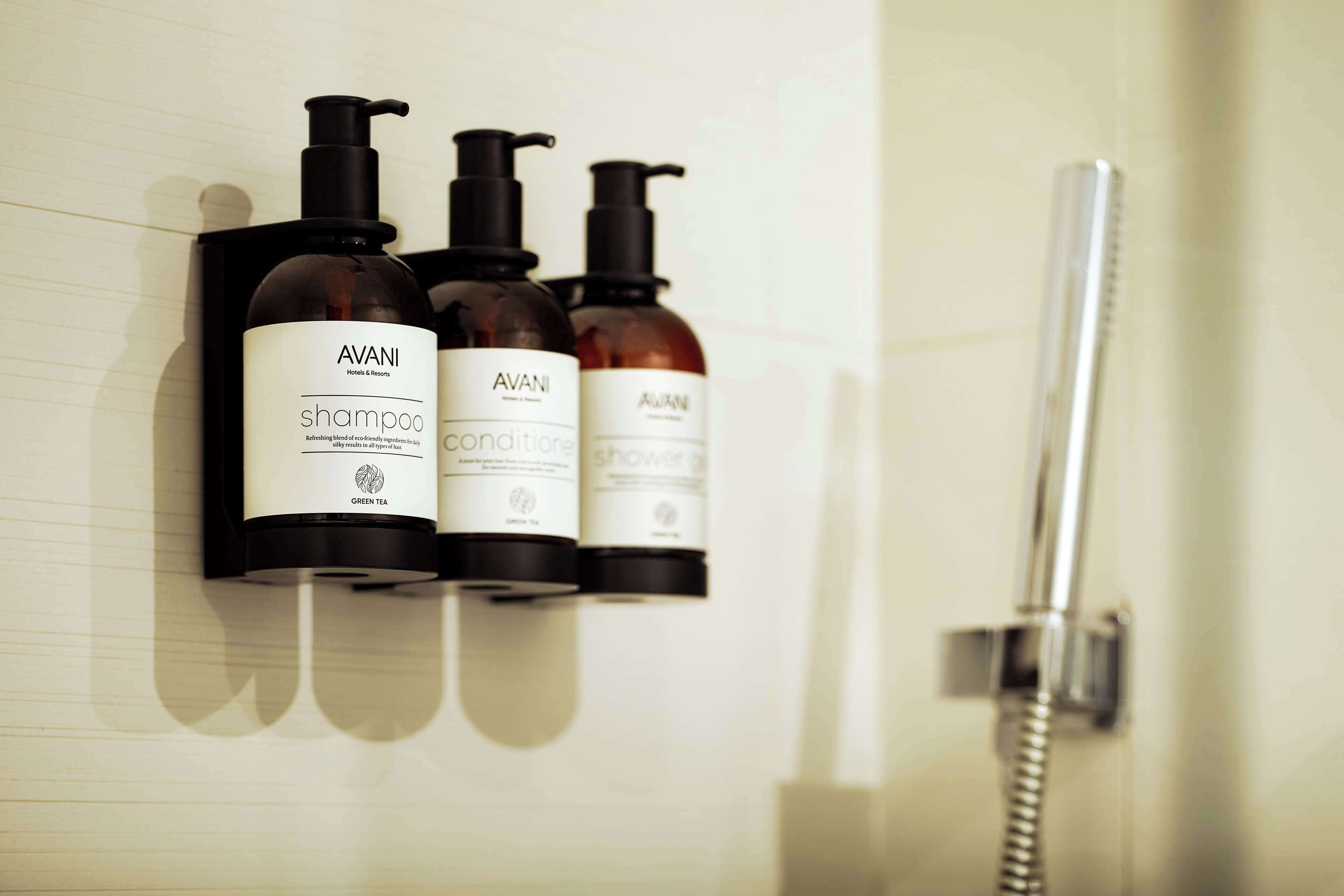 Une salle de bain équipée de trois flacons de la marque AVANI : un shampoing, un après-shampoing et un gel douche.