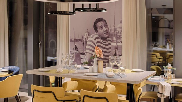 Uma área de refeições com uma mesa posta para dois, cadeiras e uma luminária pendente moderna.