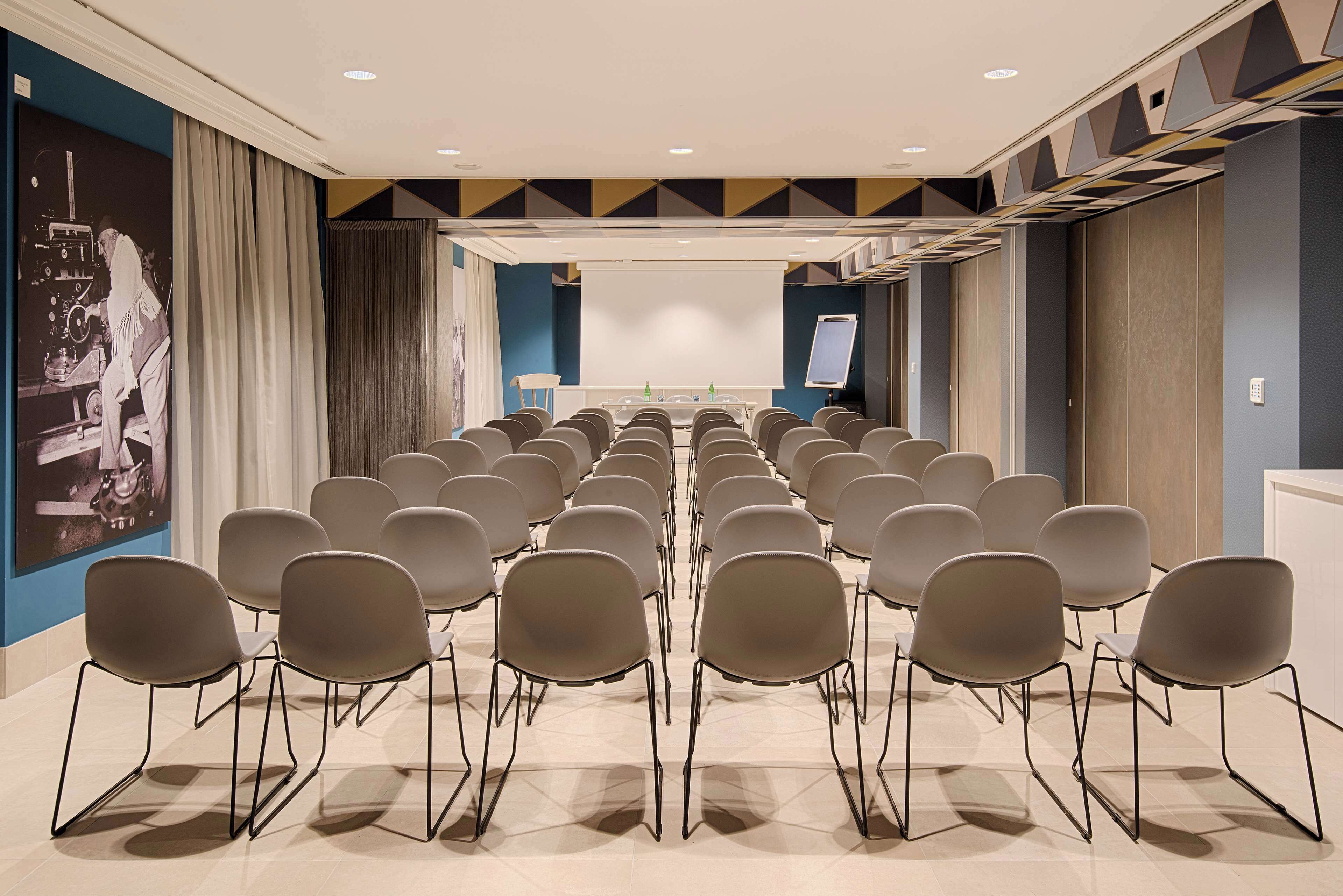 A conference room with rows of chairs, a projector screen, and a whiteboard.