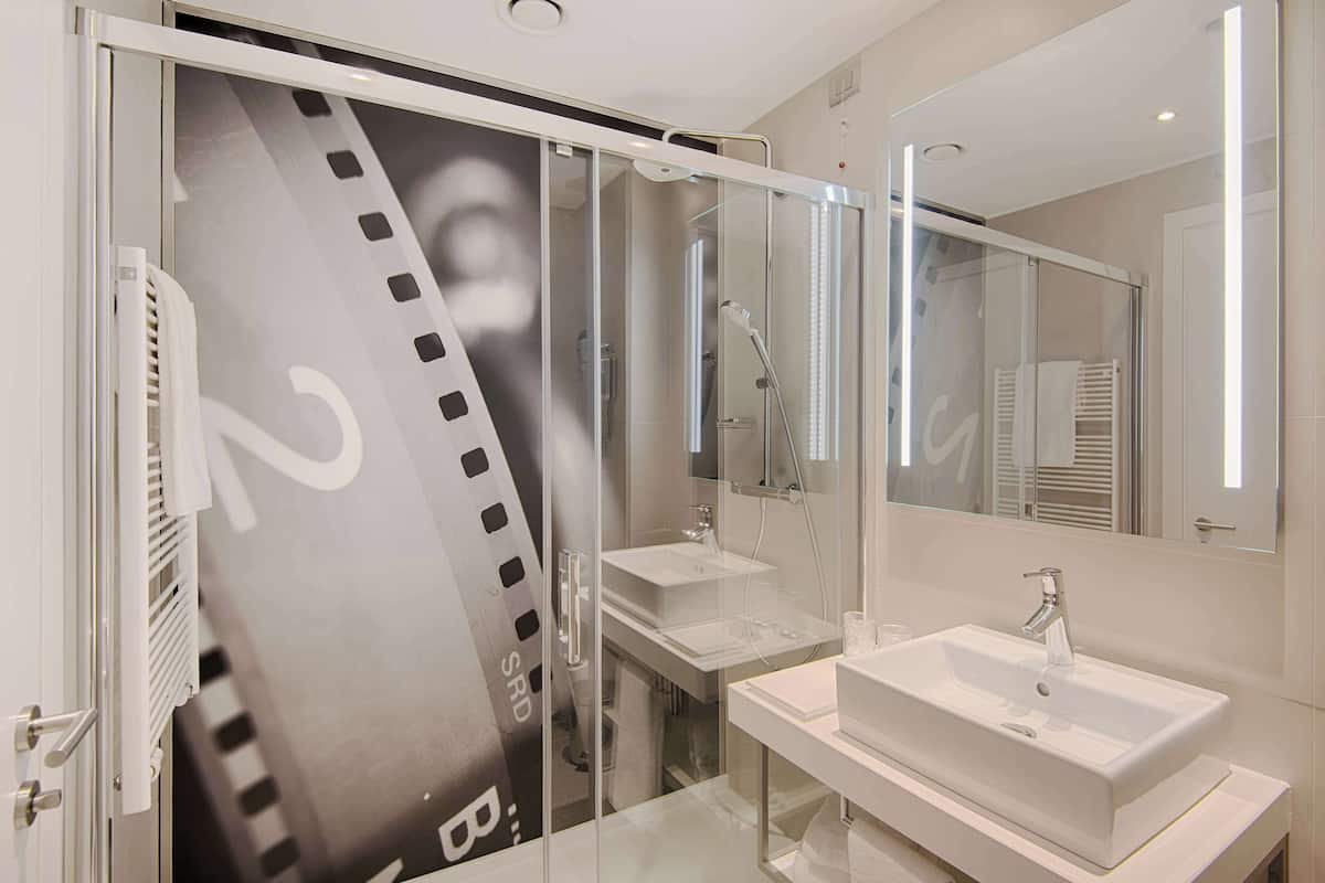 A modern bathroom with a glass shower enclosure, a large mirror, and a white sink.