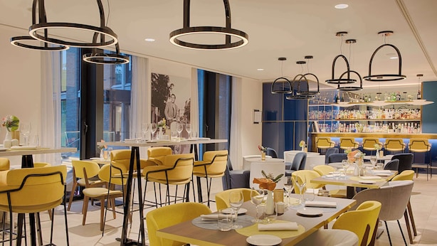 A modern dining area with yellow chairs, round tables, and pendant lighting. - Avani Rio Novo Venice Hotel (Venice)