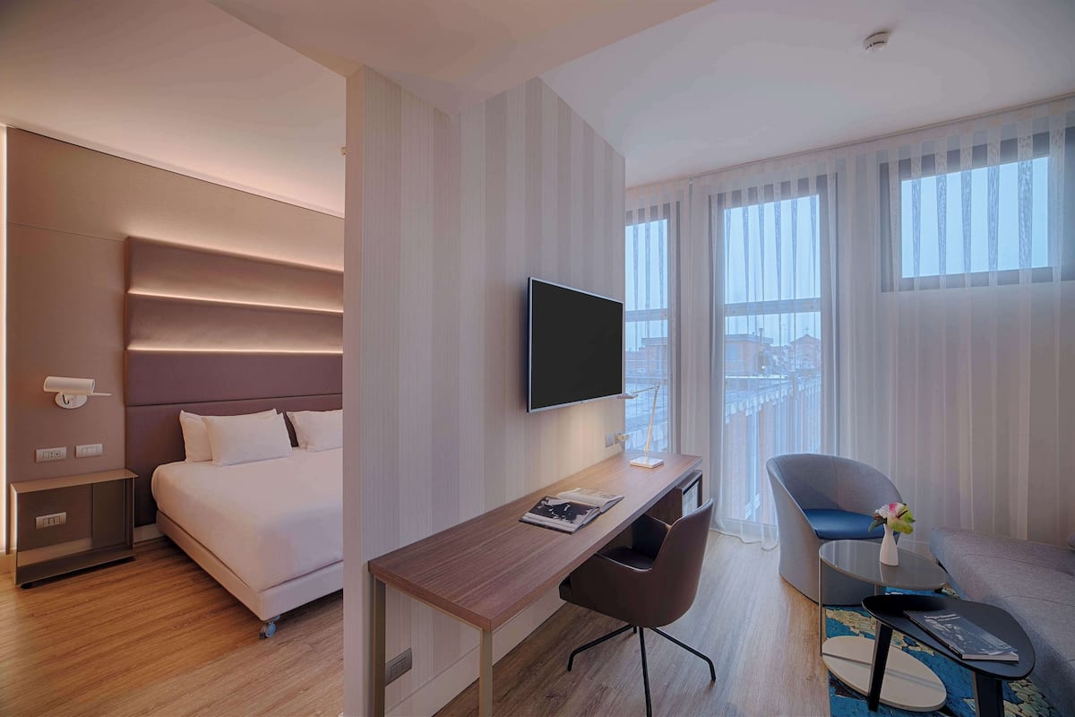 A hotel room with a bed, a desk, a chair, a TV, and a window with curtains.