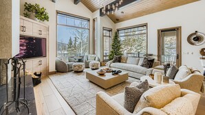 A spacious living room with a large flat-screen TV, a wooden coffee table, and a cozy seating area with sofas and ottomans. - Lucky Star At Belle Arbor 4 Bedroom Home by RedAwning (Park City)